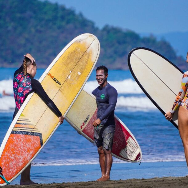 two women and a man on the beach holding surfboards