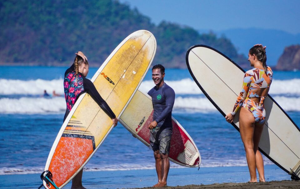 two women and a man on the beach holding surfboards